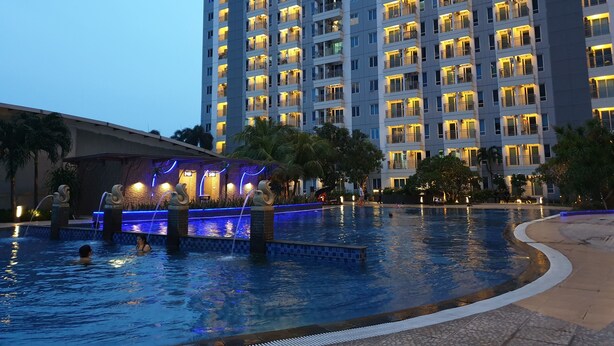 A high-rise hotel with multiple balconies and a swimming pool area with water features. - Cosmy Orchard Apartment (Surabaya)