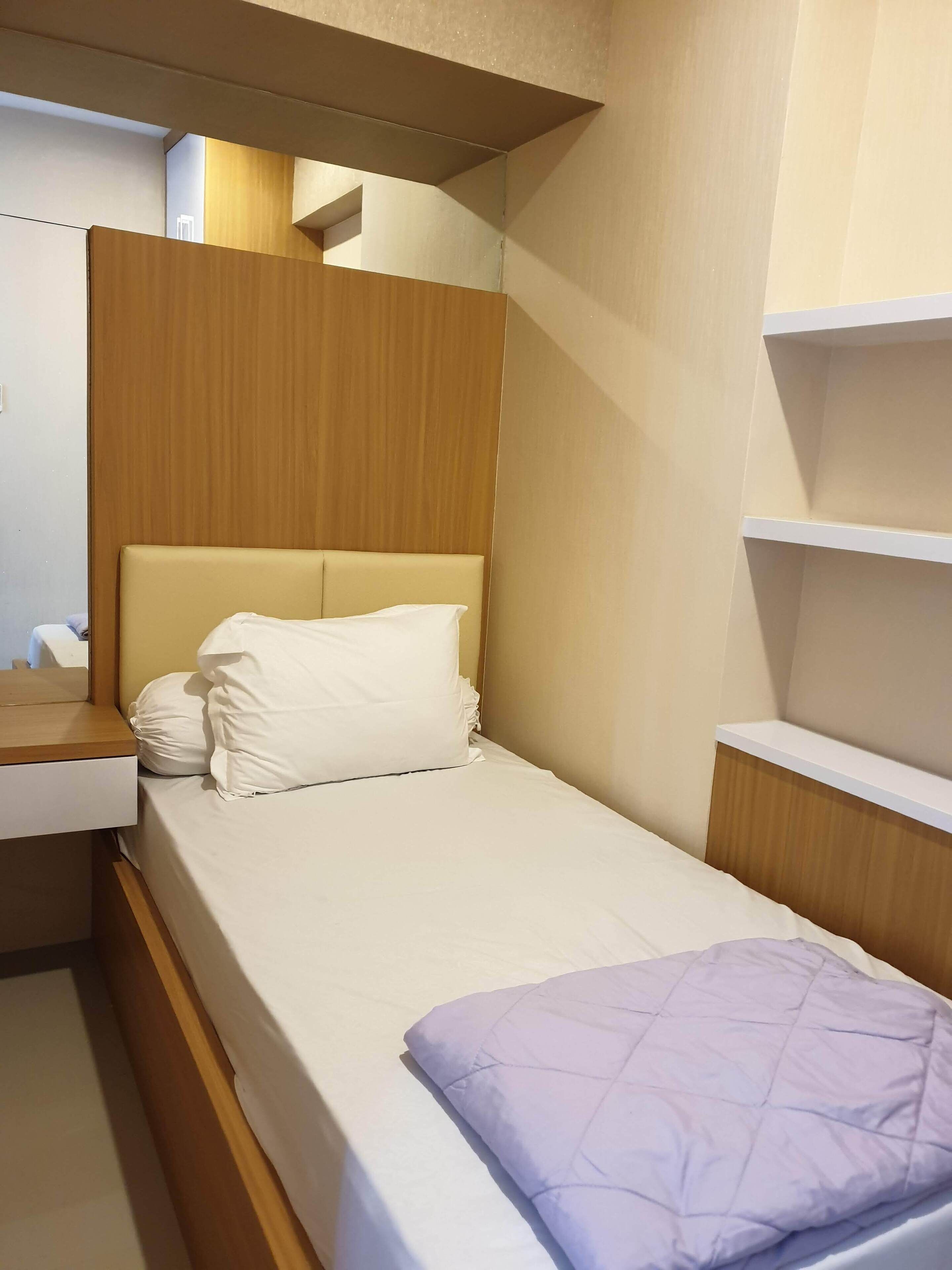 A small, neatly made bed with a wooden headboard and a single white pillow.