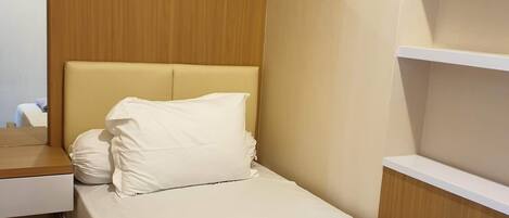 A small, neatly made bed with a wooden headboard and a single white pillow.