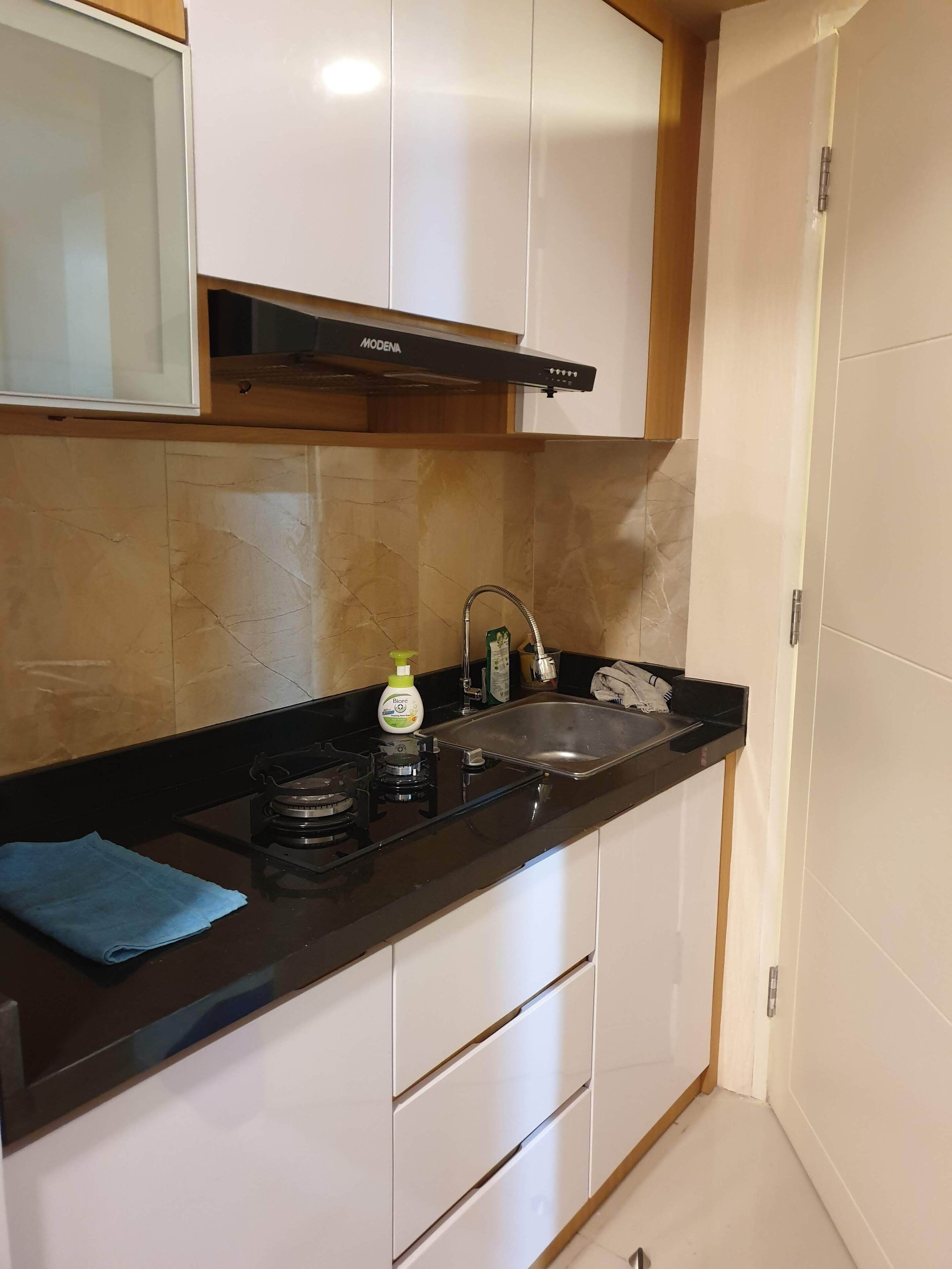 A compact kitchen with a black countertop, white cabinets, a stainless steel sink, and a Modena range hood.