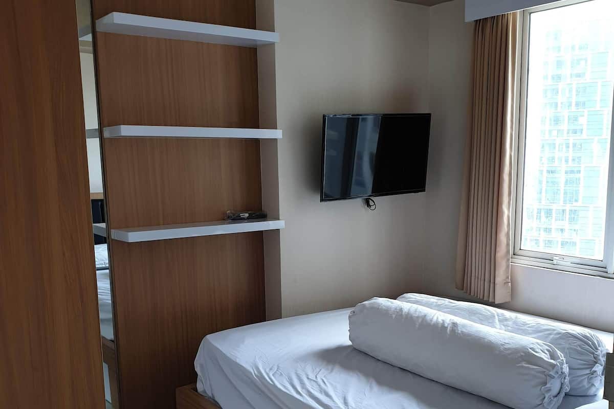 A bedroom with a bed, a TV mounted on the wall, and a window with curtains.