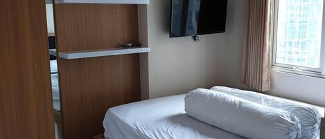 A bedroom with a bed, a TV mounted on the wall, and a window with curtains.