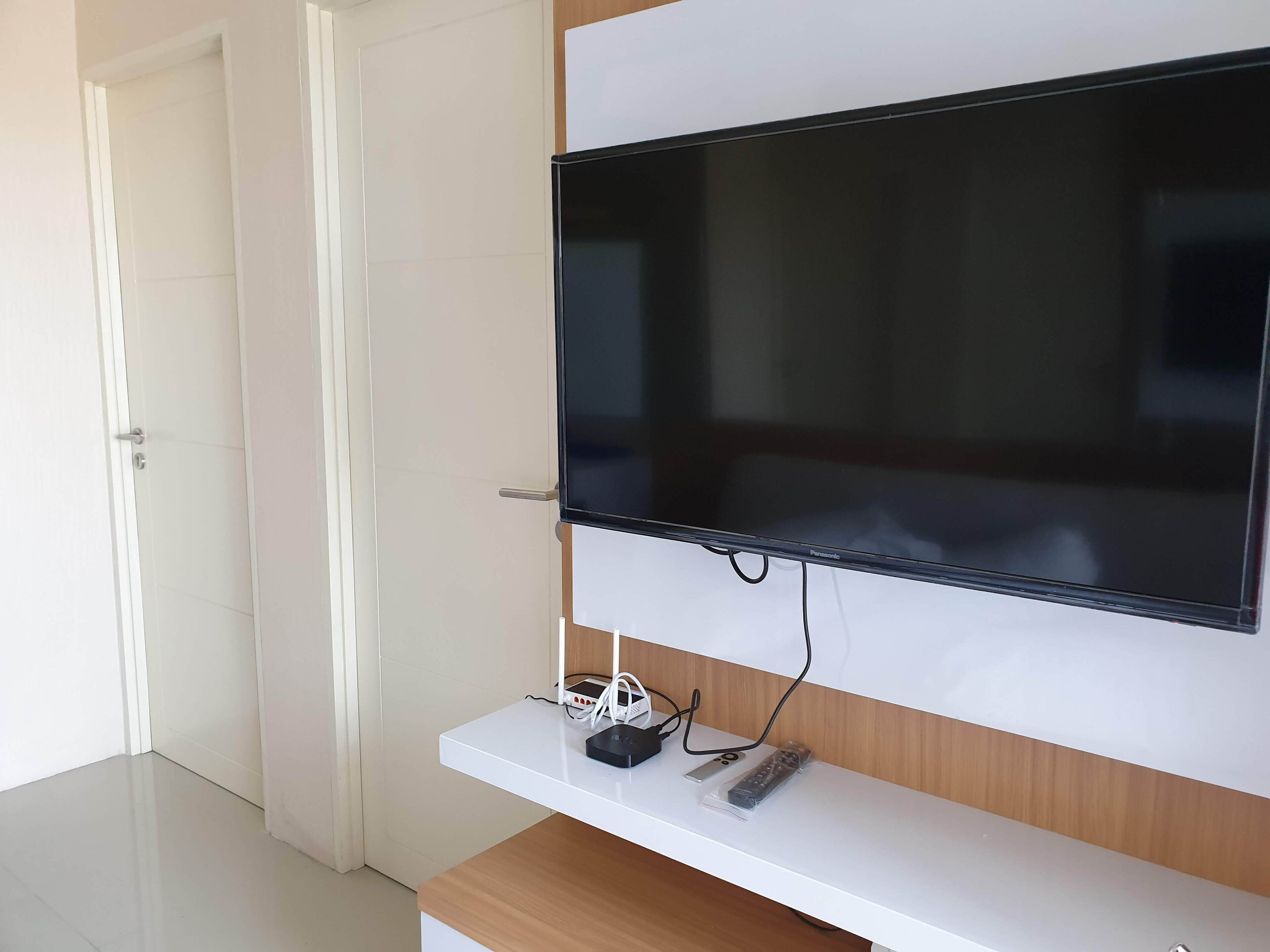 A modern living room with a flat-screen TV mounted on a white wall, a wooden cabinet below, and a door to the left.