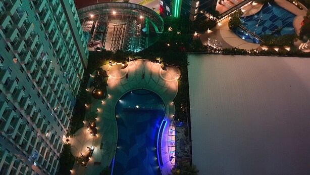 Un hotel de gran altura con zona de piscina, que incluye un elemento acuático circular y un área de descanso cubierta.