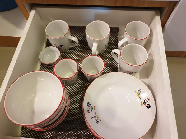 A drawer containing white mugs with red rims and plates with black and red designs.