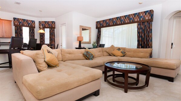 A living room with a beige sectional sofa, a glass coffee table, and patterned curtains. - Je43024 - Reunion Resort - 4 Bed 2 Baths Villa (Kissimmee)