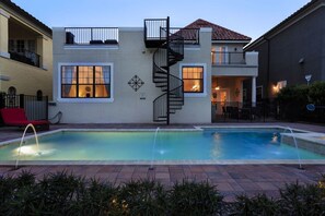 Uma casa de dois andares com piscina, escadaria em espiral e área de varanda com móveis de exterior.
