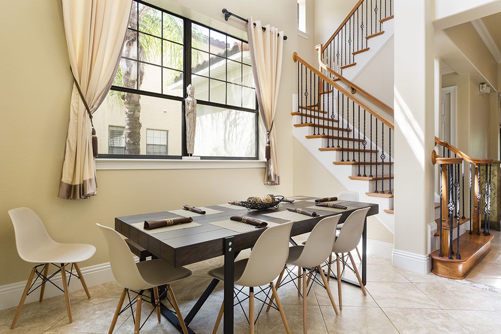 A dining area with a large table, chairs, and a view of a staircase.