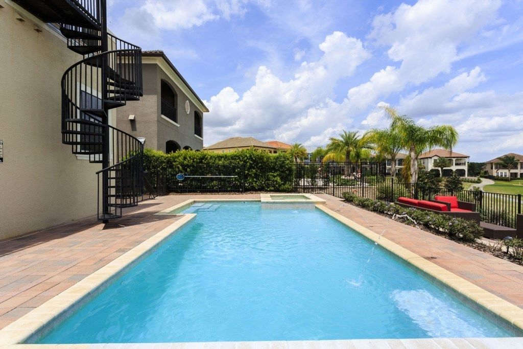 Una piscina rectangular con solárium empedrado, rodeada por una valla y palmeras.