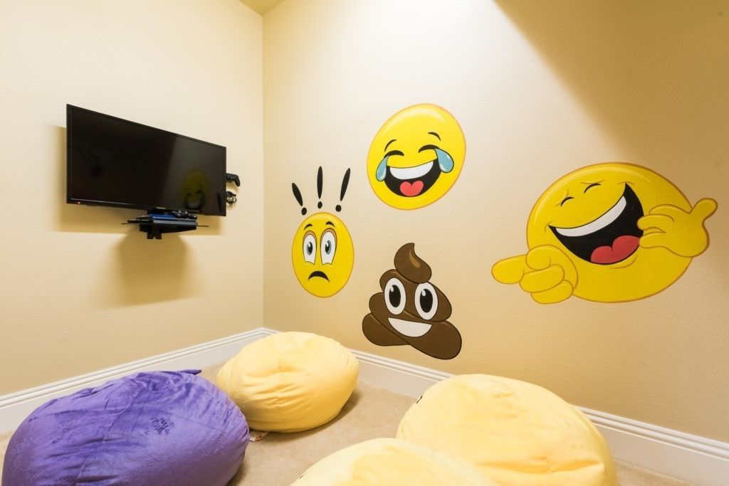 Ein Zimmer mit Flachbildfernseher an der Wand, Sitzsäcken und Wandstickern mit verschiedenen Smileys.