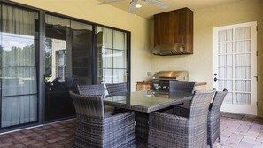 A patio with a glass table and wicker chairs, a grill, and a sliding glass door.