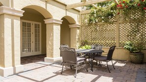 Eine Terrasse im Freien mit Tisch, Stühlen, einem Gitterzaun und Blumentöpfen.