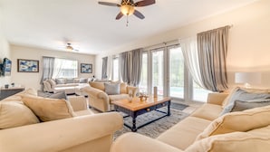 Ein geräumiges Wohnzimmer mit beigefarbenen Sofas, einem Holztisch und einem Deckenventilator.