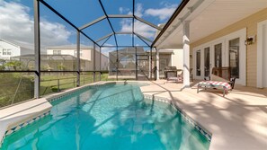 Ein Schwimmbecken mit Glasumrandung, umgeben von einer Terrasse mit Liegestühlen und einer Grillanlage.