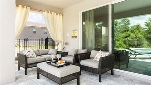 A balcony with wicker furniture, a glass door, and a view of a house and greenery.