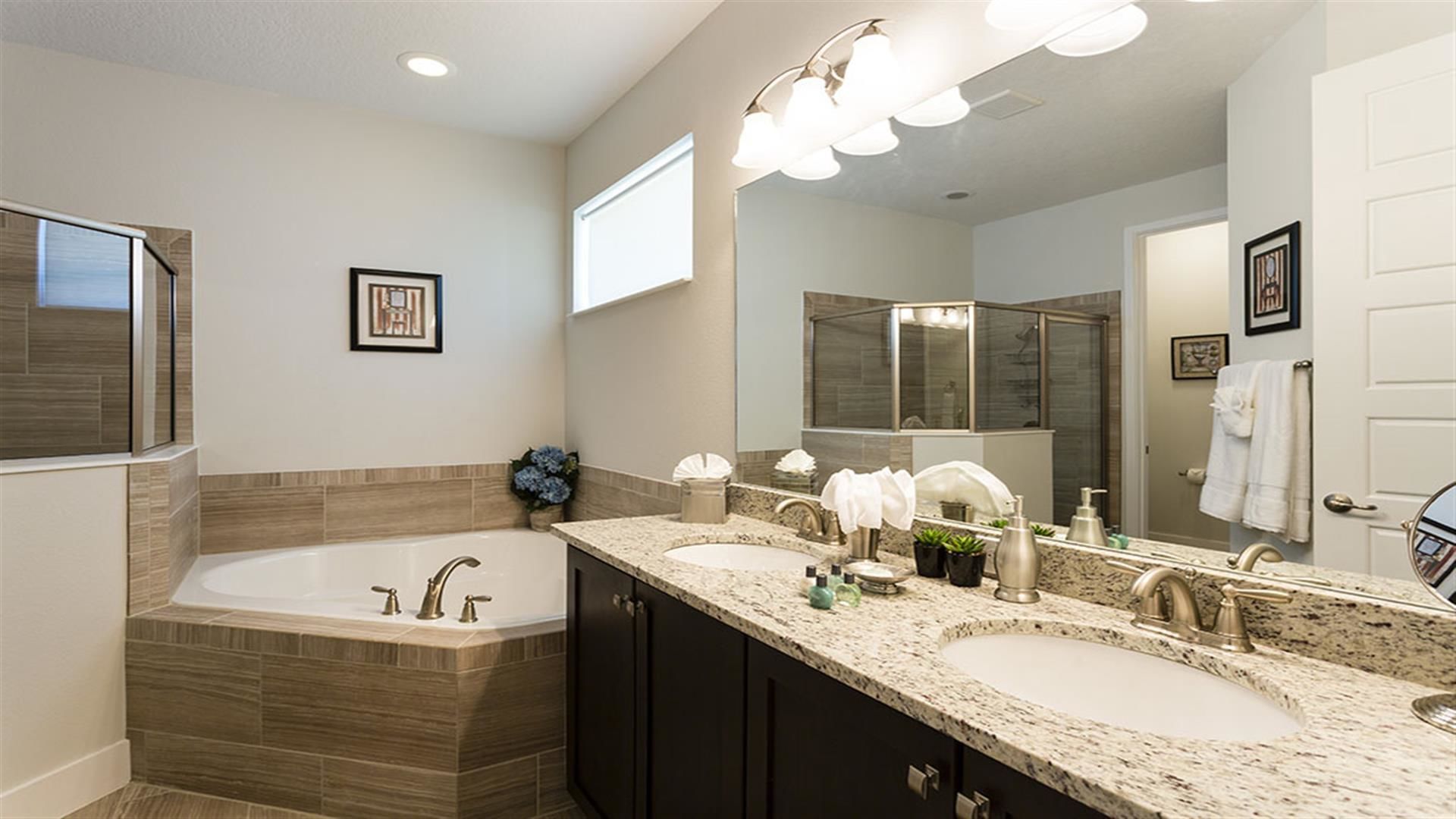 A modern bathroom with a large bathtub, two sinks, dark cabinets, and a large mirror.