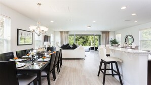 A modern kitchen with a dining area, a white sofa, and a view of the outdoors.