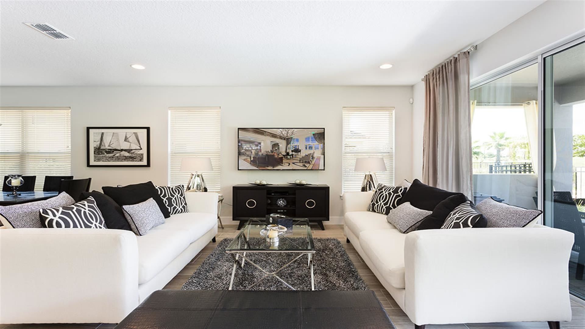 A modern living room with a white sofa set, a glass coffee table, and a flat-screen TV mounted on the wall.