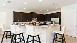 A modern kitchen with dark wood cabinets, a stainless steel refrigerator, and a central island with bar stools.