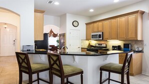 A kitchen with a central island, wooden cabinets, a microwave, and a clock on the wall. - Je62762 - Reunion Resort - 4 Bed 2 Baths Villa (Kissimmee)