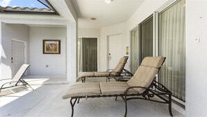 A covered patio with two lounge chairs and a door leading to a room. - Je62762 - Reunion Resort - 4 Bed 2 Baths Villa (Kissimmee)