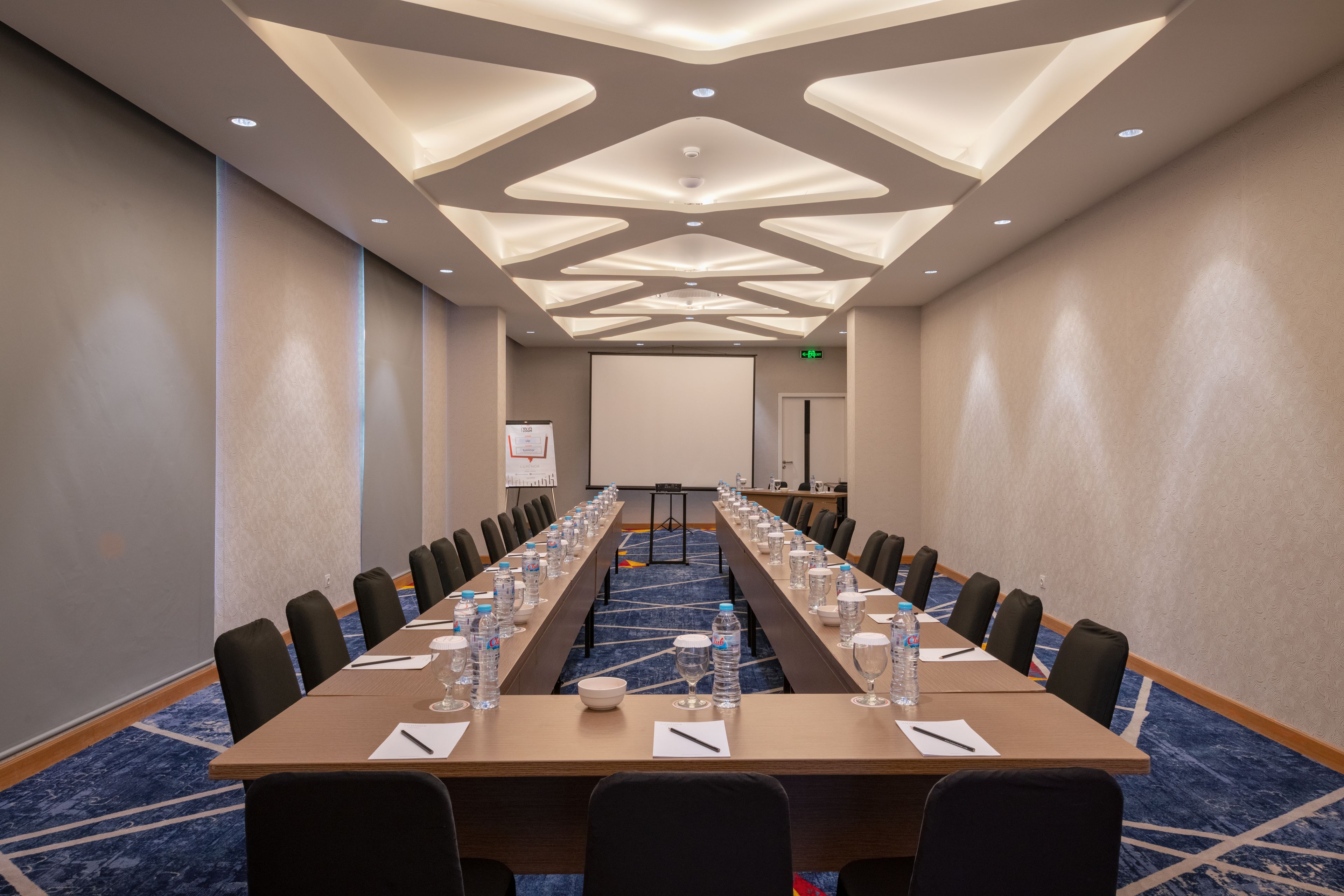 A conference room with a long table, chairs, water bottles, and a projector screen.