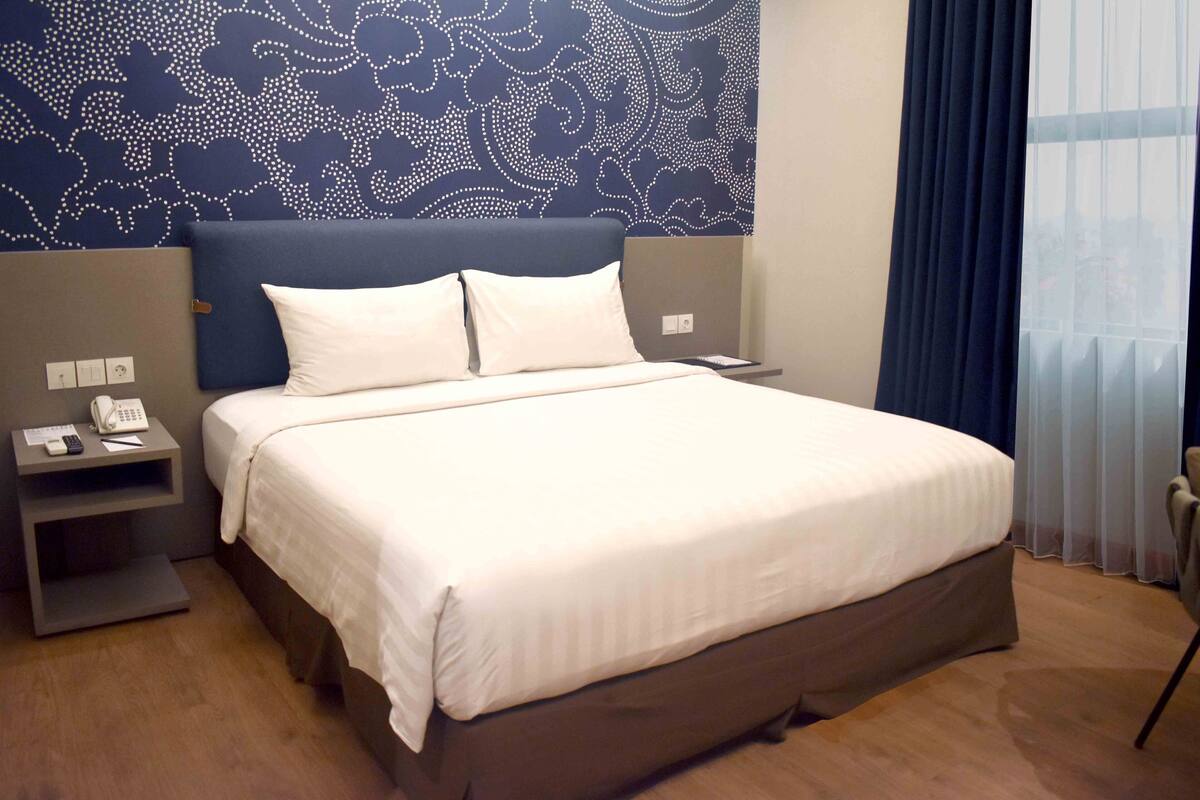A hotel room with a large bed, a bedside table with a phone, and a patterned wall.