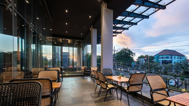 A restaurant with outdoor seating, large windows, and a view of the cityscape.