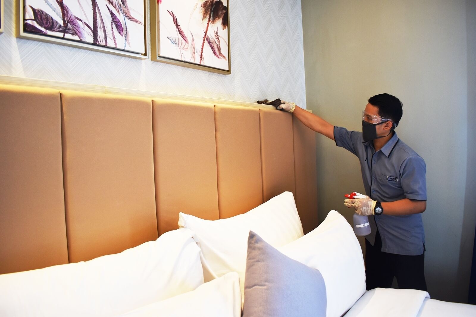 A hotel room with a large, padded headboard, white bedding, and artwork on the wall.