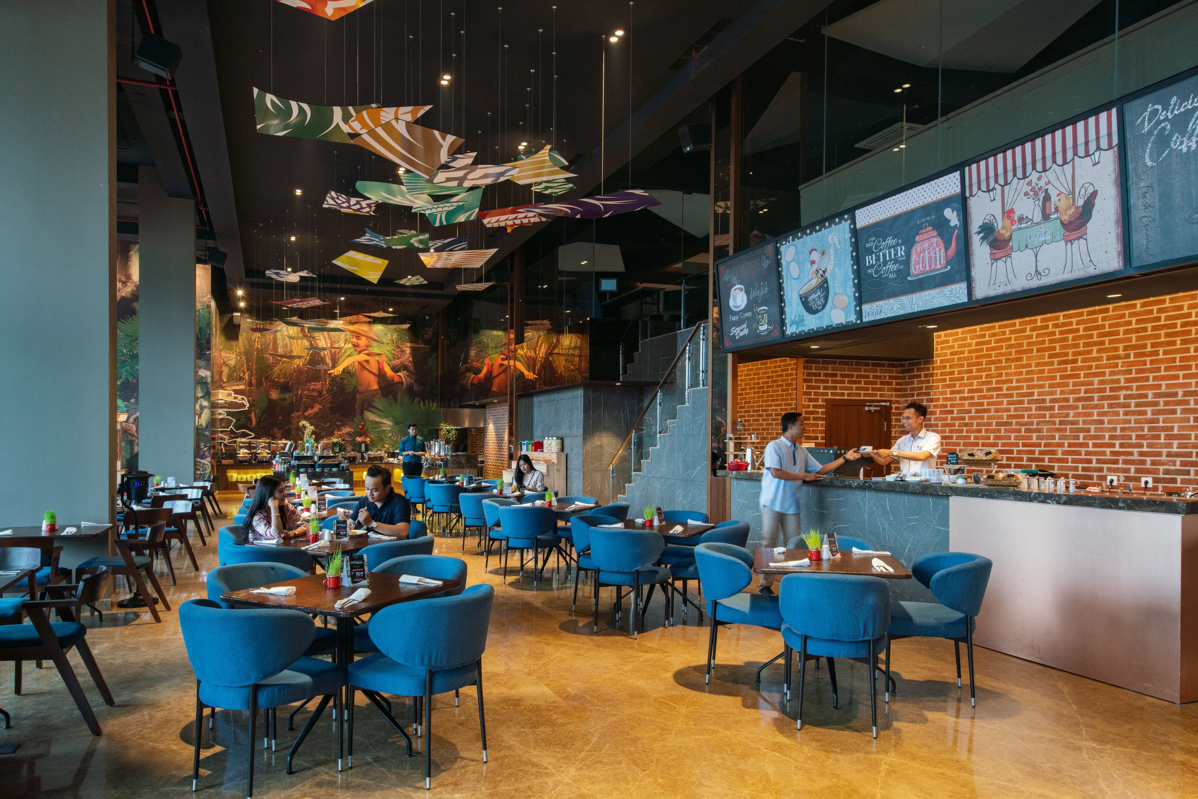 Un restaurant moderne avec des chaises bleues, un mur en briques et un comptoir où le personnel sert les clients.