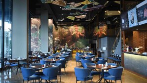 A spacious restaurant with blue chairs and tables, a large mural on the wall, and hanging decorations.