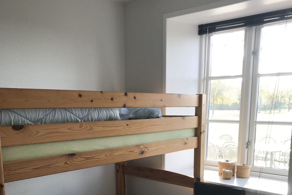 A bunk bed with a desk and chair, a window with blinds, and a view of the outside.