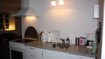 Una cocina con estufa, horno, lavaplatos y encimera. Hay utensilios, una cafetera y un adorno en la encimera.