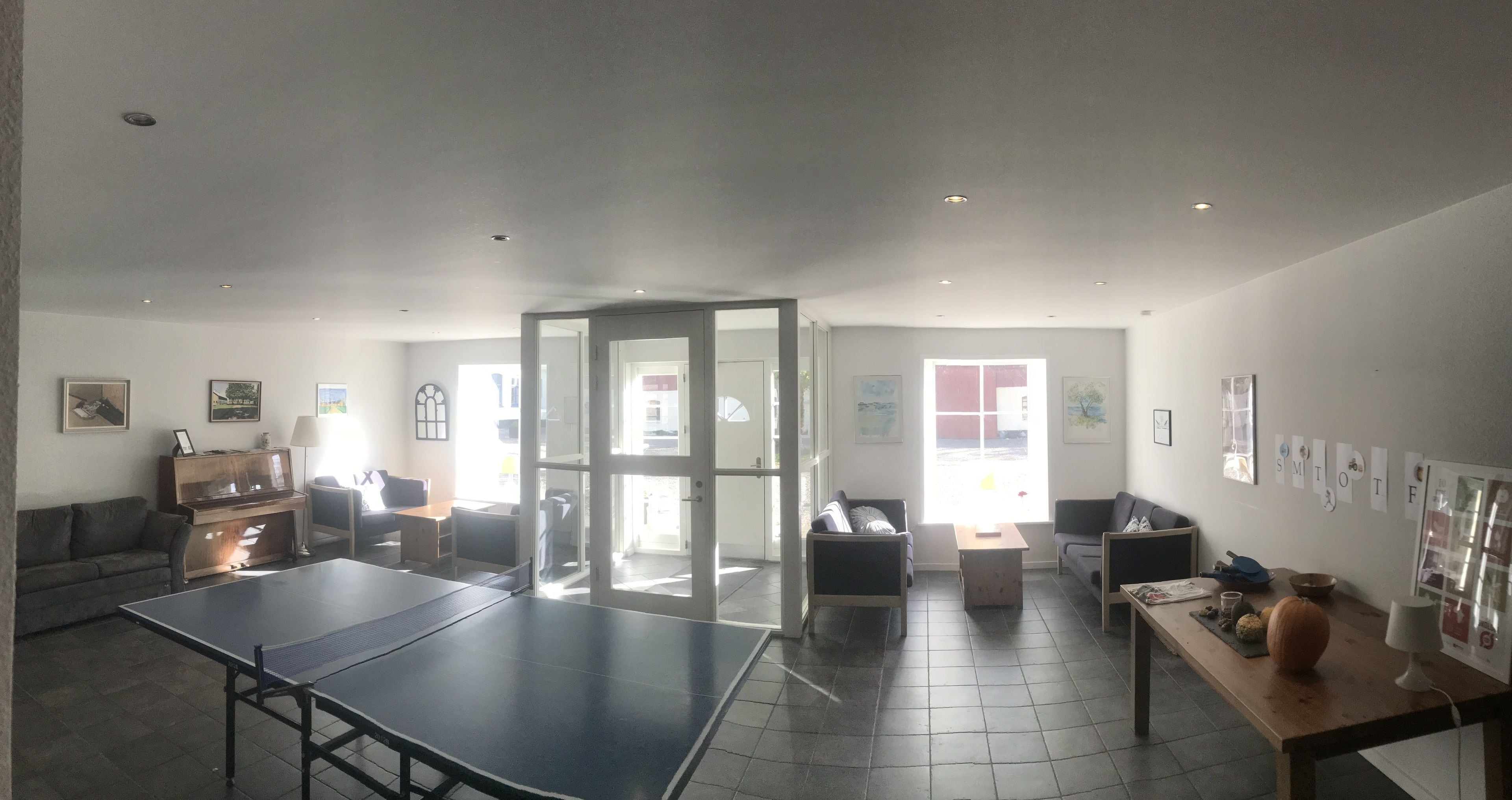 Àmplia zona d'estar amb taula de ping-pong, sofàs, un piano i una finestra gran.