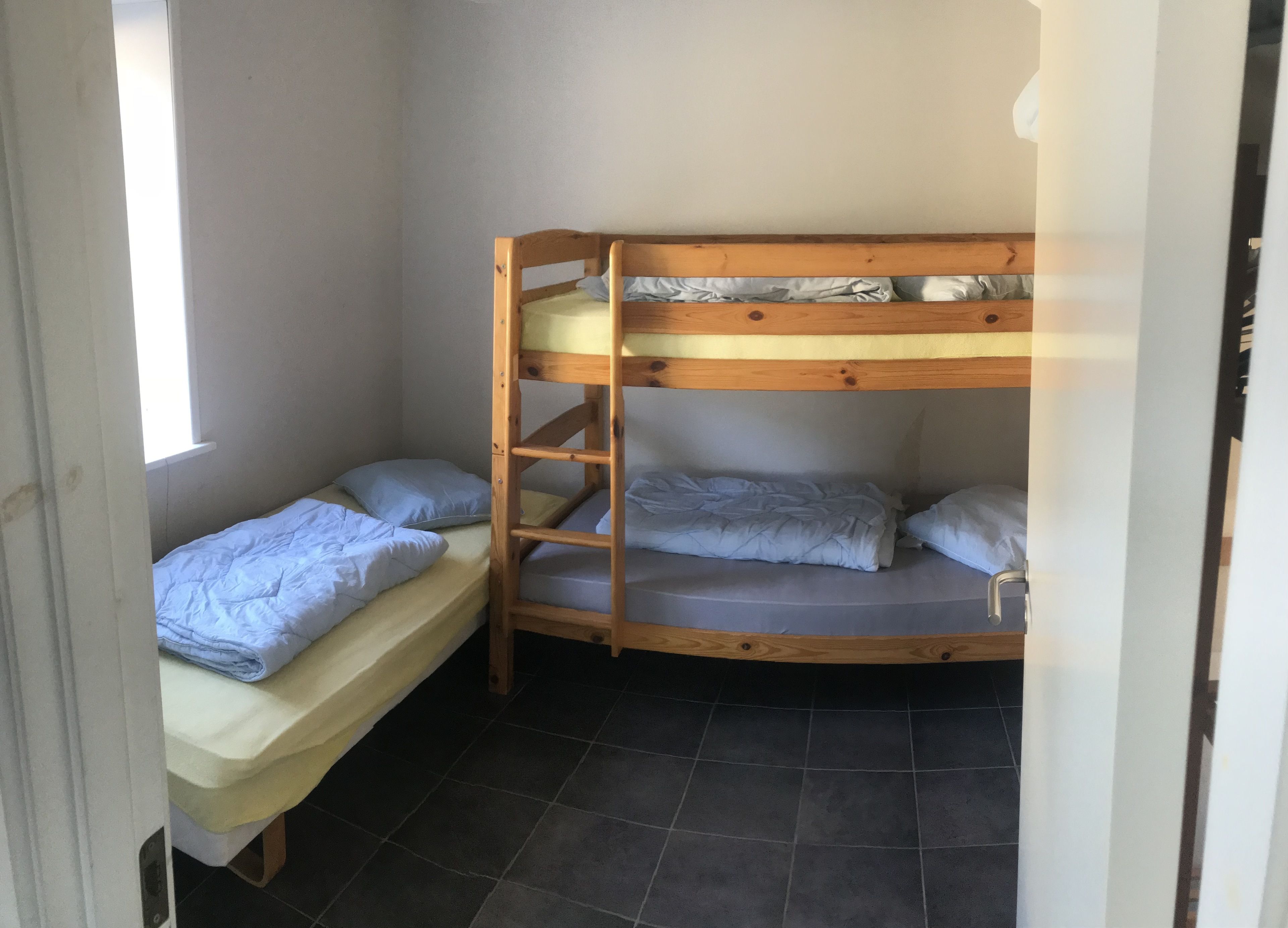 Ein Schlafraum mit Etagenbett, einer Leiter, zwei Einzelbetten und einem Fenster.