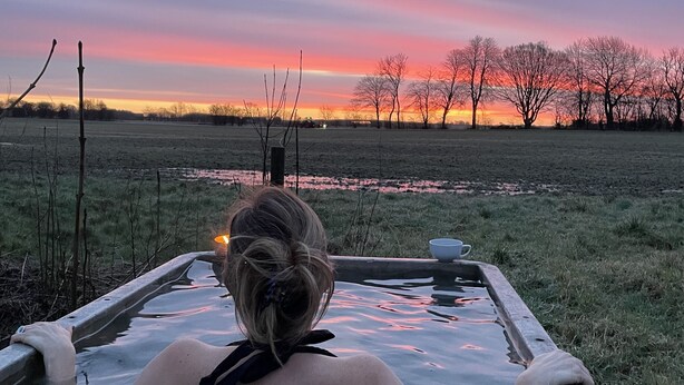 Una persona relajándose en un jacuzzi con vistas a un campo al atardecer.