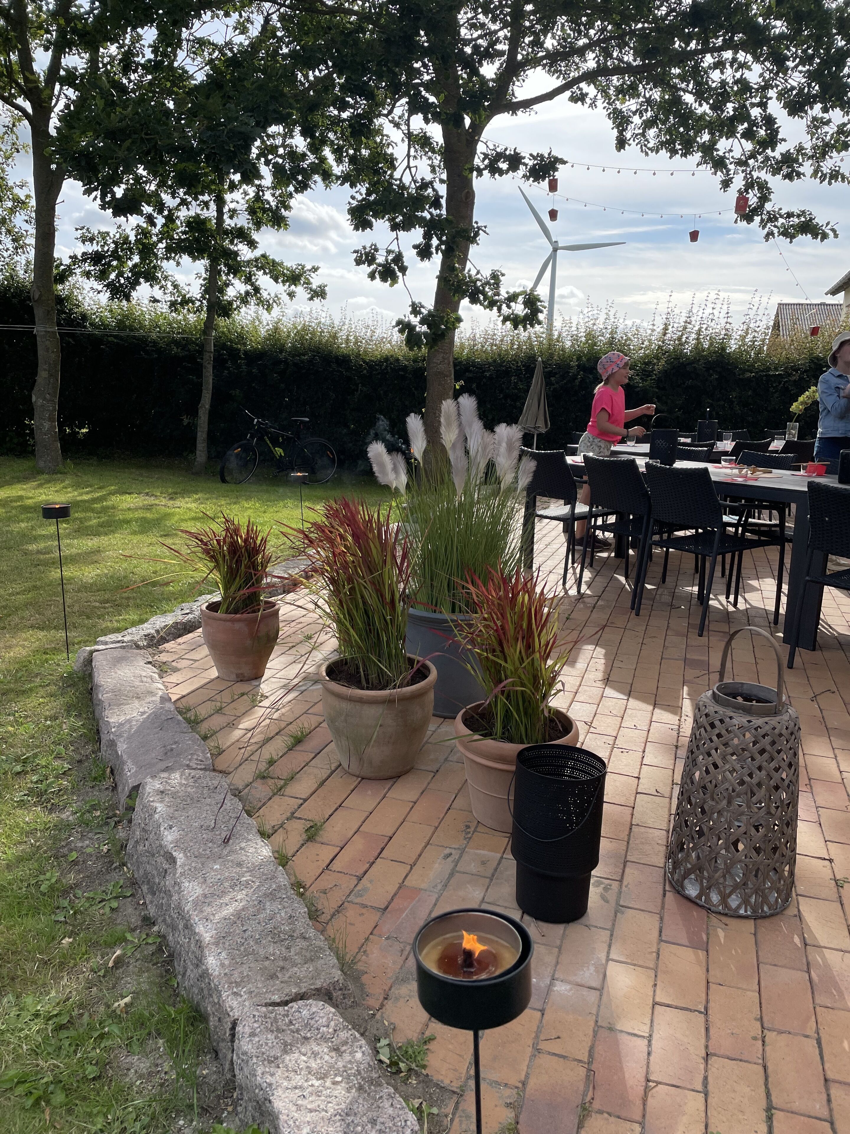 An outdoor patio area with brick flooring, potted plants, a fire pit, and outdoor furniture.