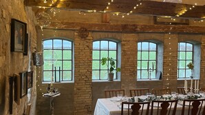 Un comedor rústico con una larga mesa dispuesta para seis personas, rodeado de paredes de ladrillo y ventanas amplias.