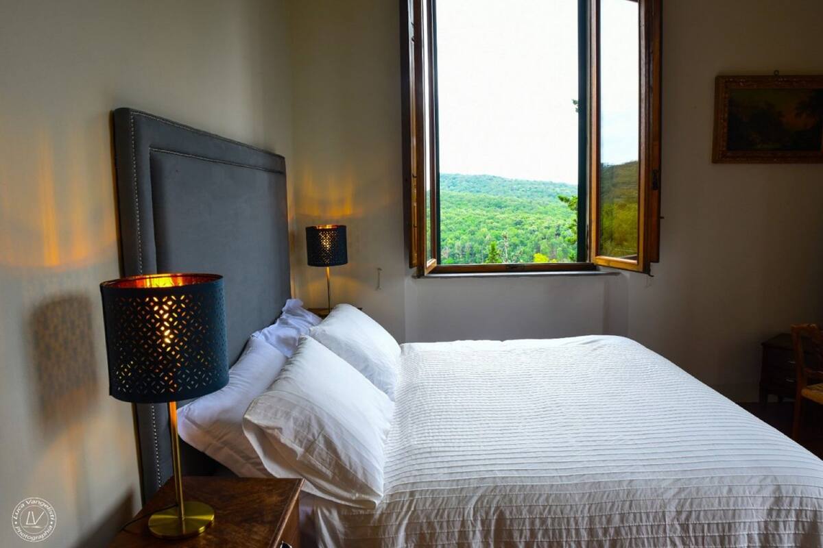 A neatly made bed with white linens, a dark headboard, and a lamp on a bedside table.