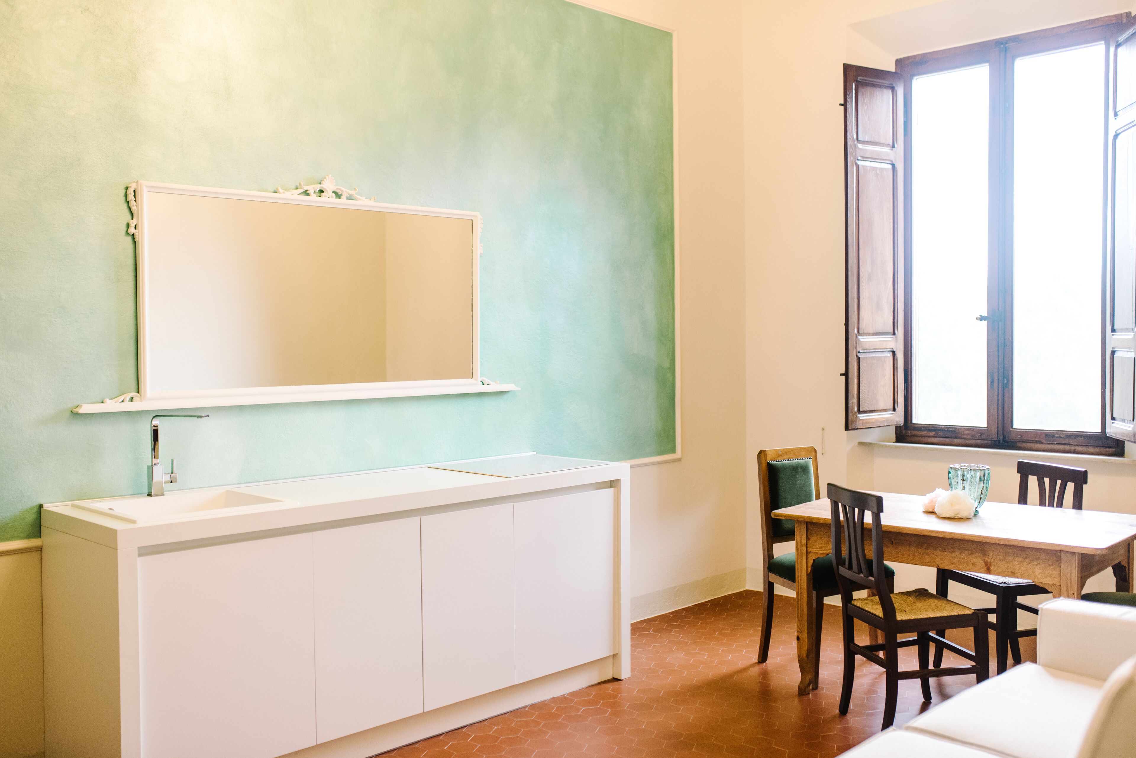 A kitchen with a white countertop, a large mirror, and a dining area with chairs and a table.