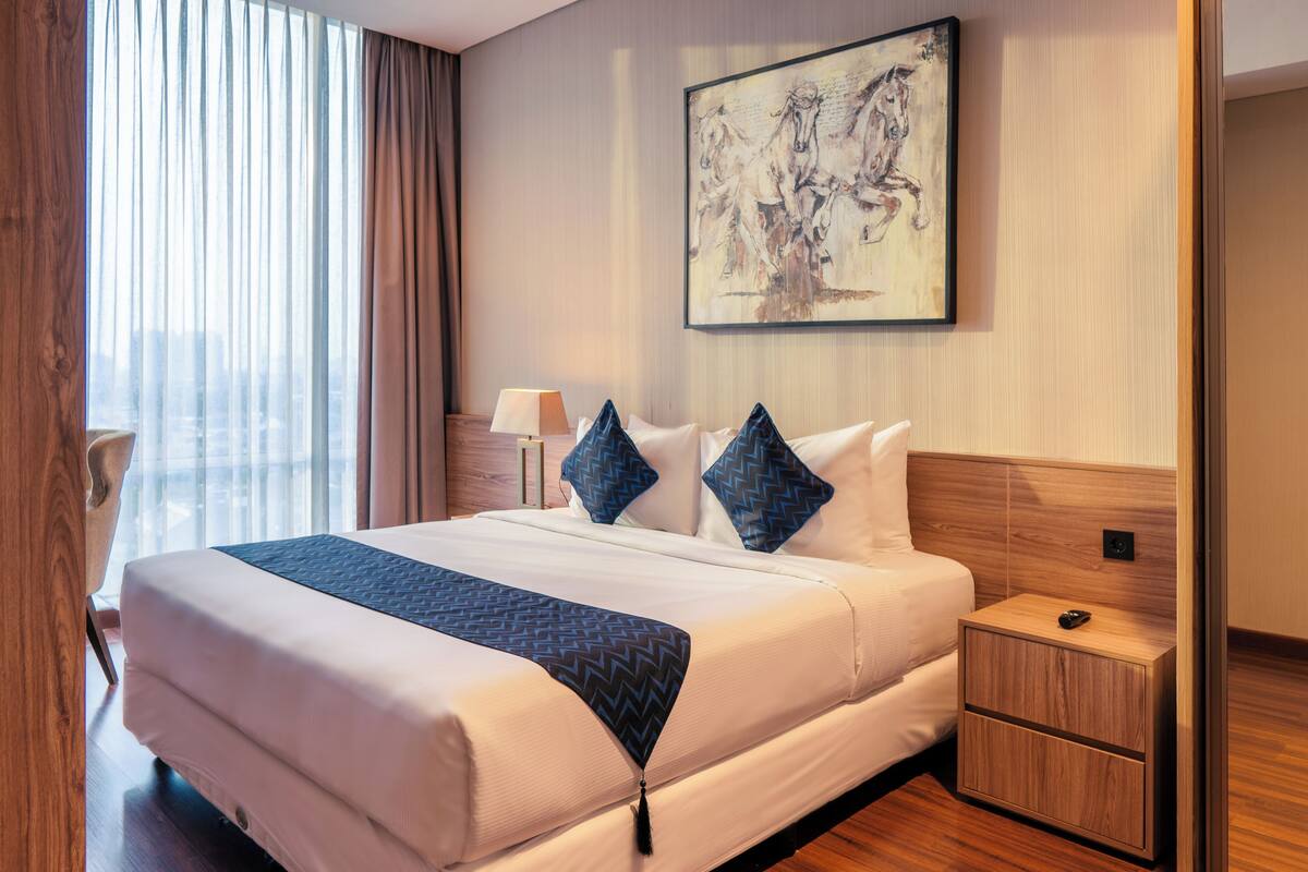 A hotel room with a large bed, a nightstand, a lamp, and a painting on the wall.