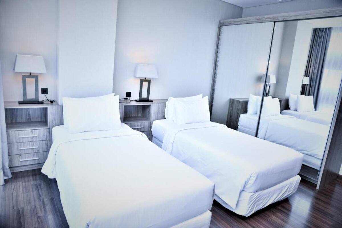 A hotel room with two beds, a large mirror, and bedside tables with lamps.