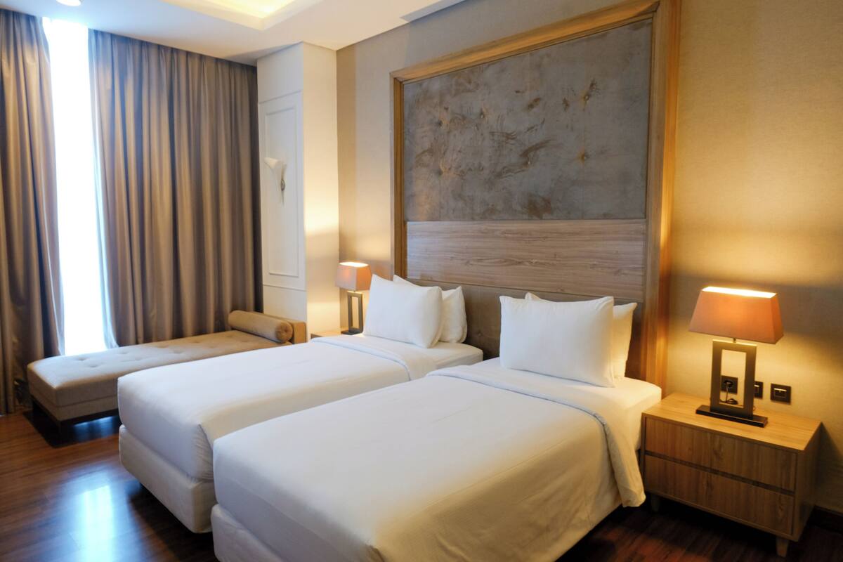 A hotel room with two beds, a large painting on the wall, and a nightstand with a lamp.