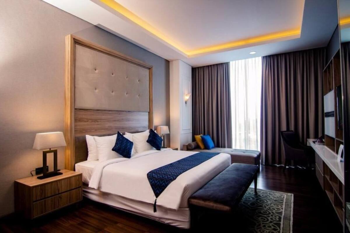 A hotel room with a large bed, bedside tables, a bench, a TV, and a view of the outdoors.