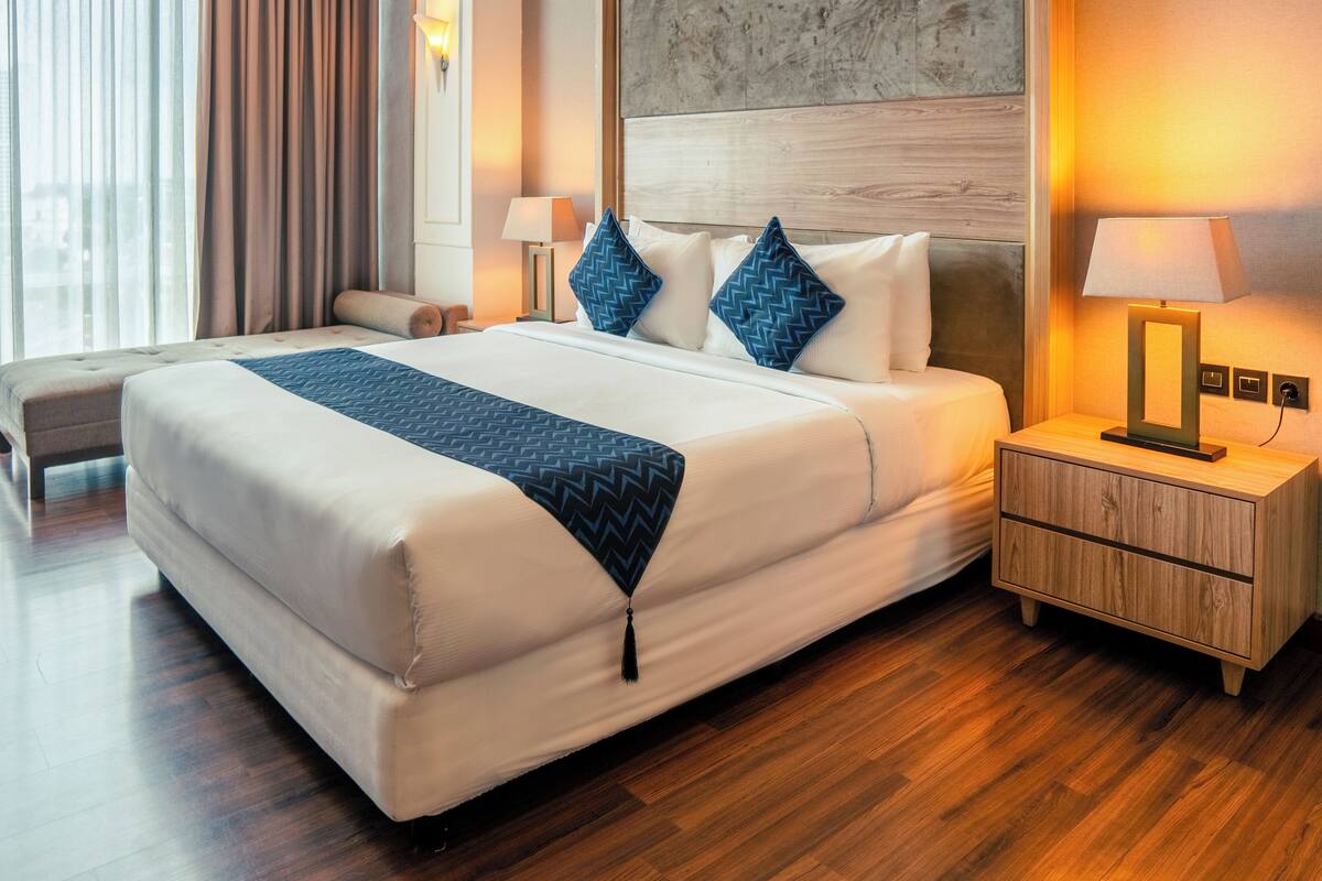 A modern hotel room with a large bed, wooden flooring, and a nightstand with a lamp.
