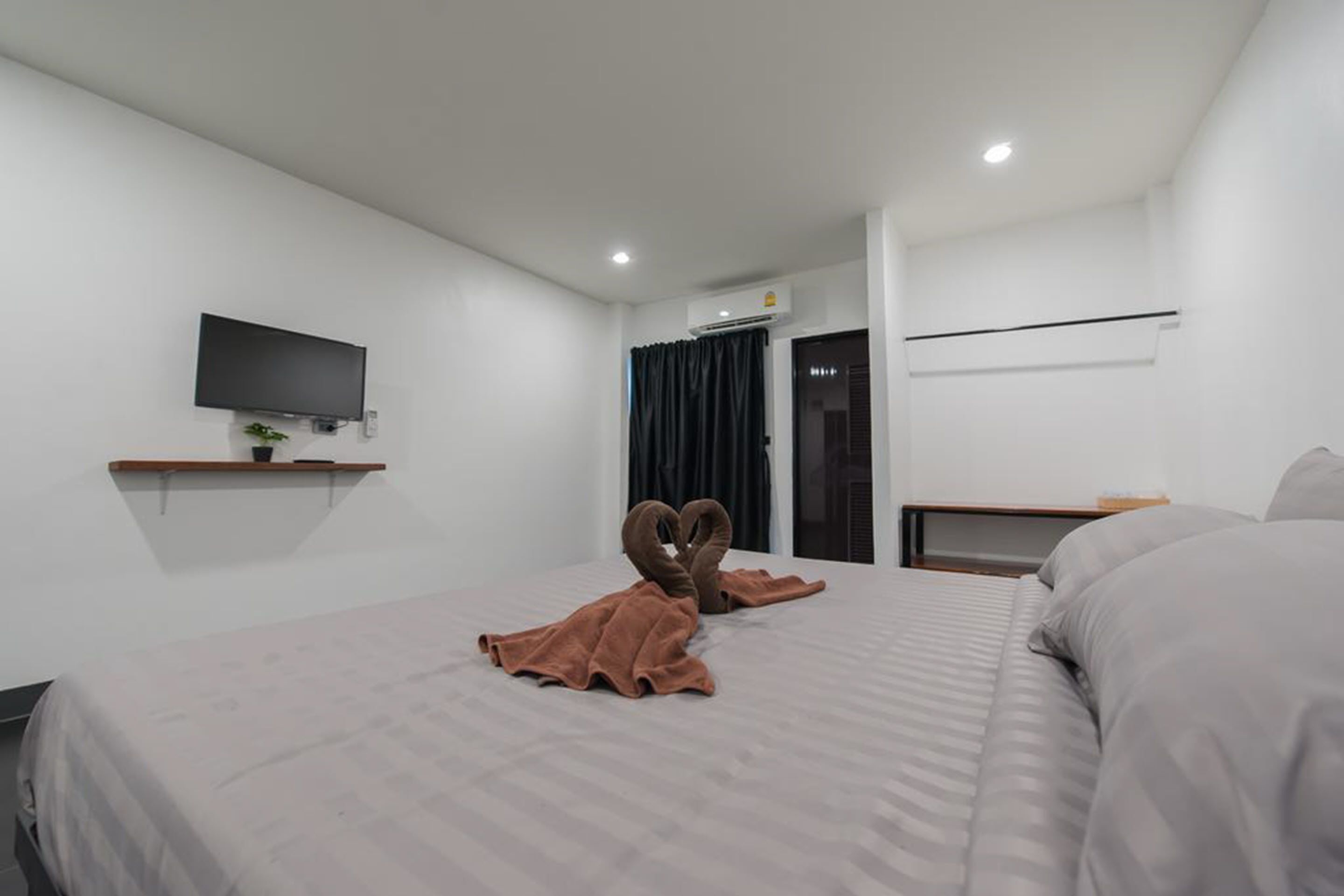 Habitación de hotel con dos camas, un televisor de pantalla plana montado en la pared, un estante con una planta y una ventana con cortinas.