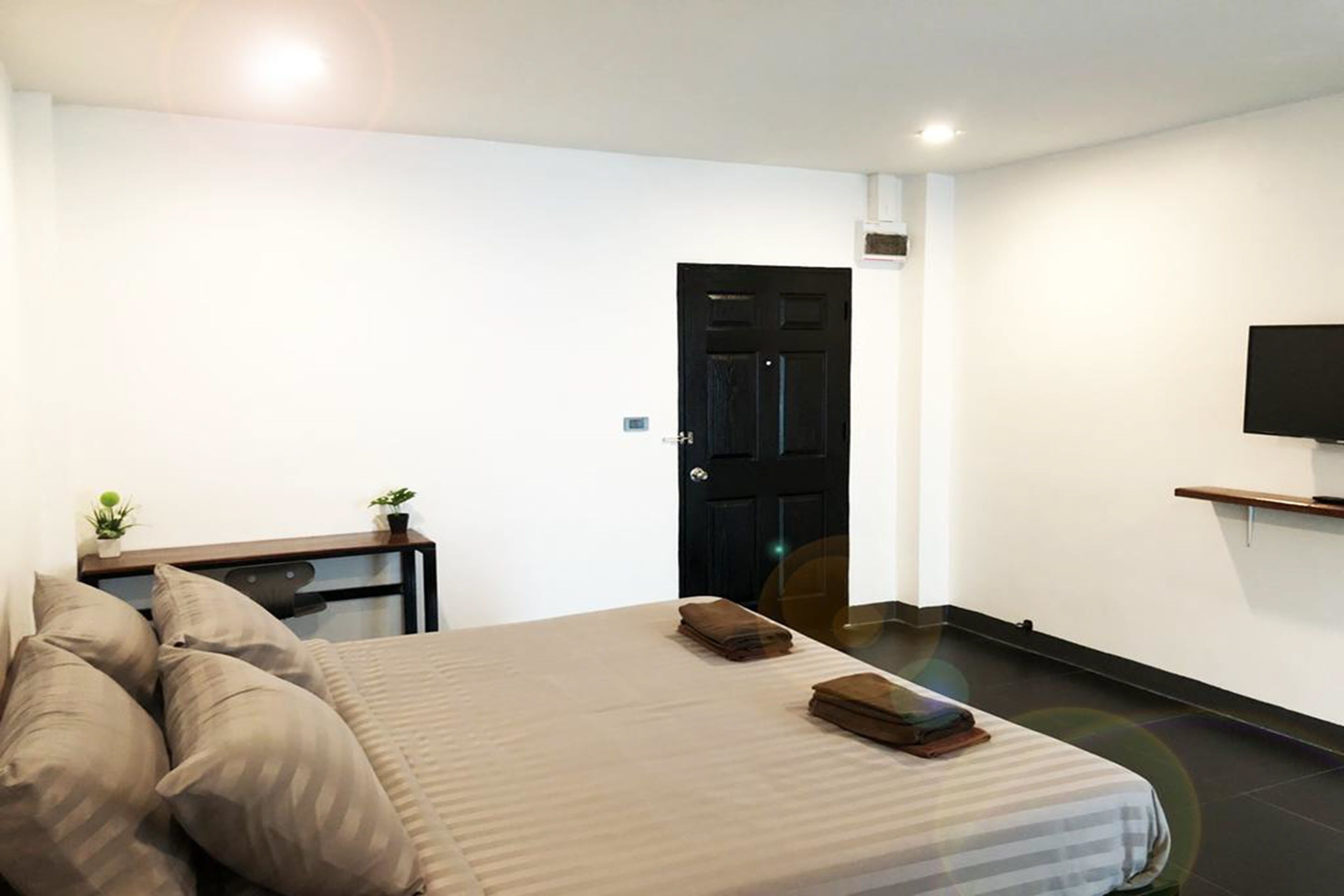 Camera d'albergo moderna con un letto, una televisione, un tavolino con una pianta e una porta nera.