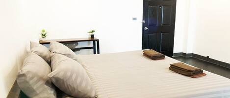 A single bed with a striped bedspread, two pillows, a small bedside table with a plant, and a folded towel on the bed.