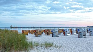 Beach huts arranged in rows on a sandy beach with a pier in the background. - Carat Residenz-Apartmenthaus (Groemitz)