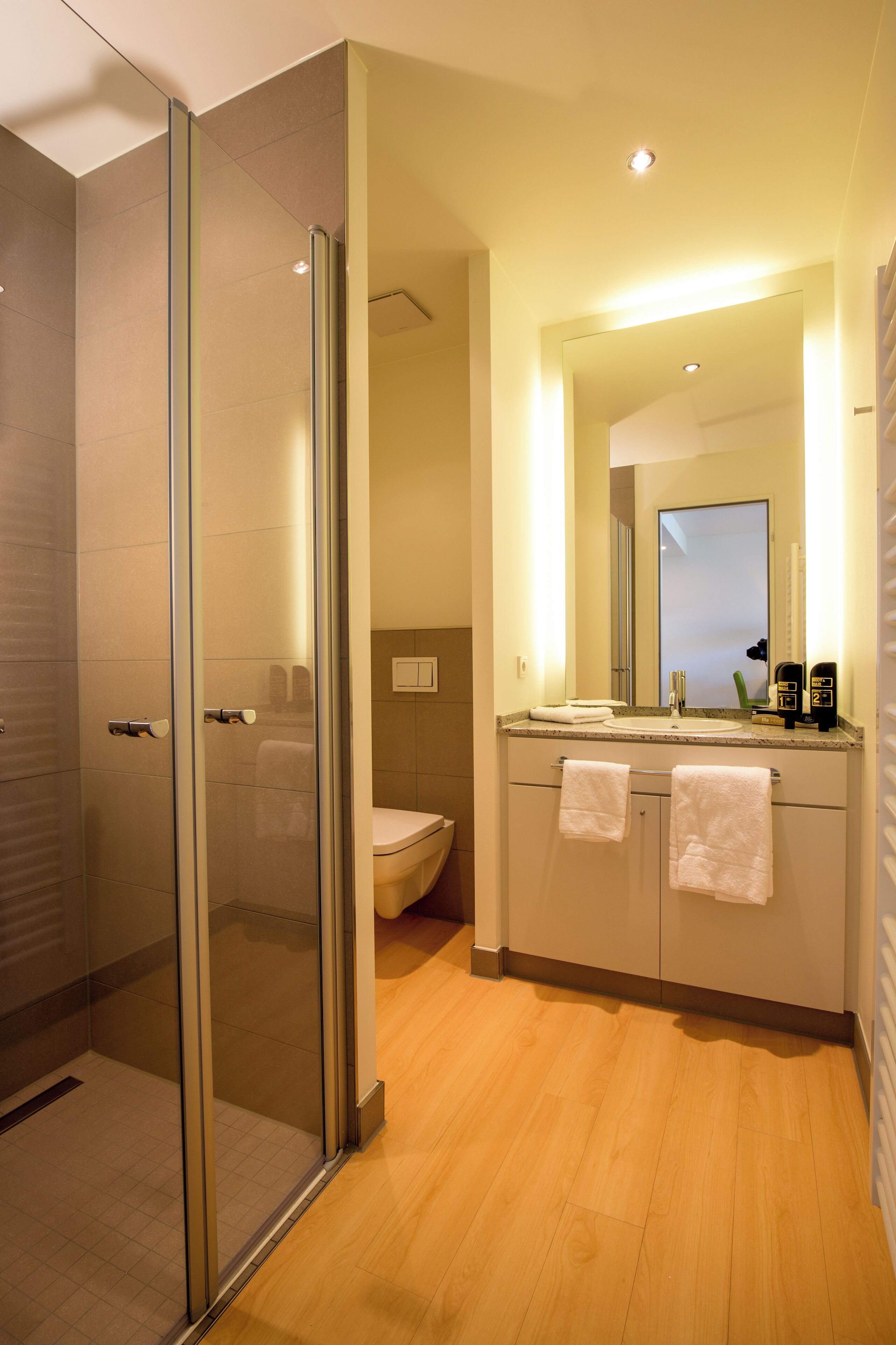A modern bathroom with a glass shower enclosure, a sink with a mirror, and wooden flooring.